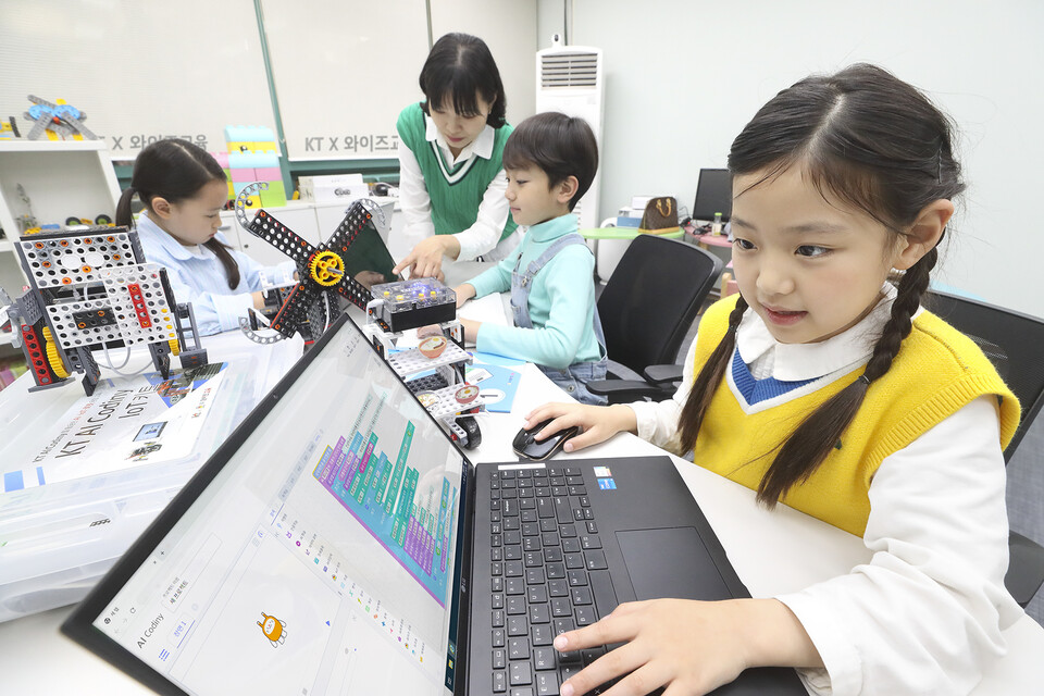 선생님이 어린 학생들에게 KT AI 코디니를 이용해 코딩과 하드웨어 융합 교육을 진행하고 있다. (사진=KT 제공)